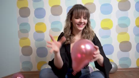 Mujer-Joven-Sentada-Alrededor-De-Globos-Y-Lanzando-Globos-A-La-Cámara-Contra-Un-Fondo-Colorido