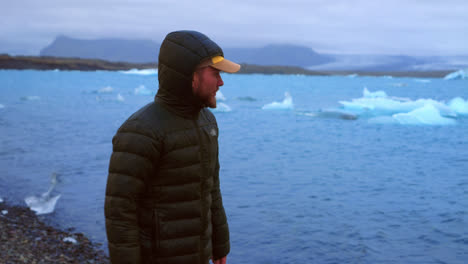 un tipo con chaqueta de invierno con capucha caminando por la laguna glaciar de jokulsarlon, islandia