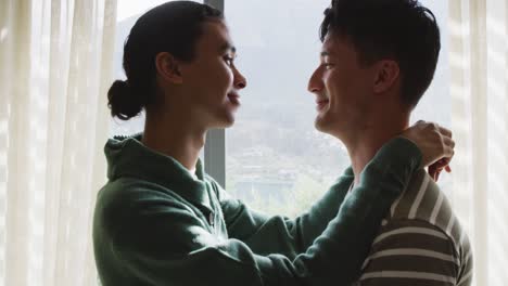 happy diverse male couple embracing and smiling in living room