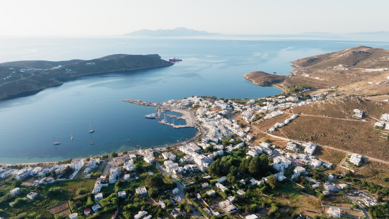 Drone pans over Livadi village and calm Serifos port with blue Aegean sea at golden sunrise
