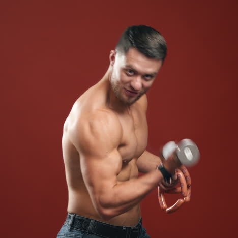 athlete in studio. topless sportsman holding sausage and dumbbell in his hands. shirtless muscular man chooses hard weight to train arm biceps.