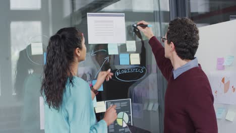 man and woman discussing over memo notes on glass board at office