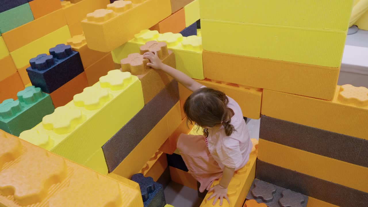 Toddler girl playing in brick playground, crawling and exploring around in indoor playroom setting, high angle static, slow motion