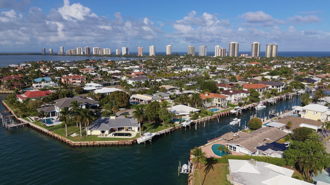 Drone shot of a boat motoring up a canal in Riviera Beach Florida north of Phil Foster Park and showing the beautiful waterfront houses and in the distance showing the oceanfront high-rise condos.