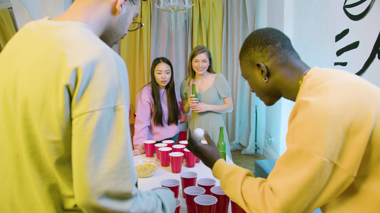 Happy multiethnic young friends playing beer pong at home