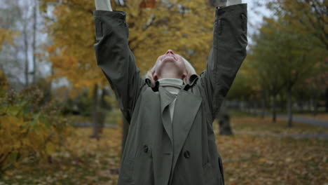 feliz mujer rubia jugando con el follaje en el clima de otoño