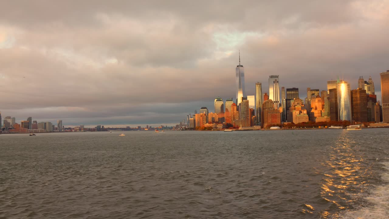 Golden hour view of NYC's Lower Manhattan from a ferry on calm waters
