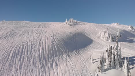 Vista-Aérea-De-Una-Moto-De-Nieve-Dejando-Huellas-En-La-Nieve-En-Revelstoke,-Columbia-Británica