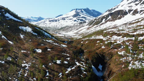 Aerial,-drone-shot-over-a-canyon,-in-a-valley,-surrounded-by-snowy-mountain-peaks-,-on-a-bright,-sunny,-summer-day,-in-the-Lyngen-alps,-North-Norway