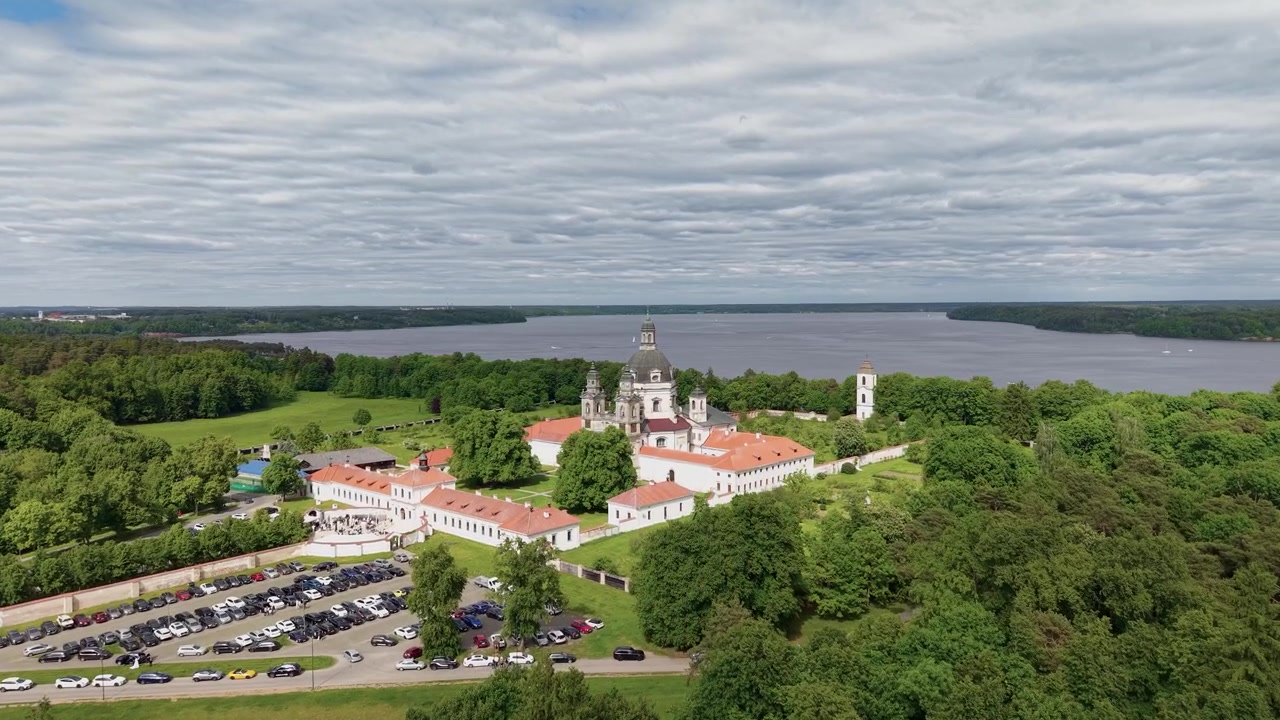 Riprese aeree dinamiche catturano il Monastero di Pazaislis a Kaunas, Lituania dall'alto, incorniciato da una foresta lussureggiante, cieli sereni e acque scintillanti del lago. Luce diurna intensa, grandangolo, nessuna persona