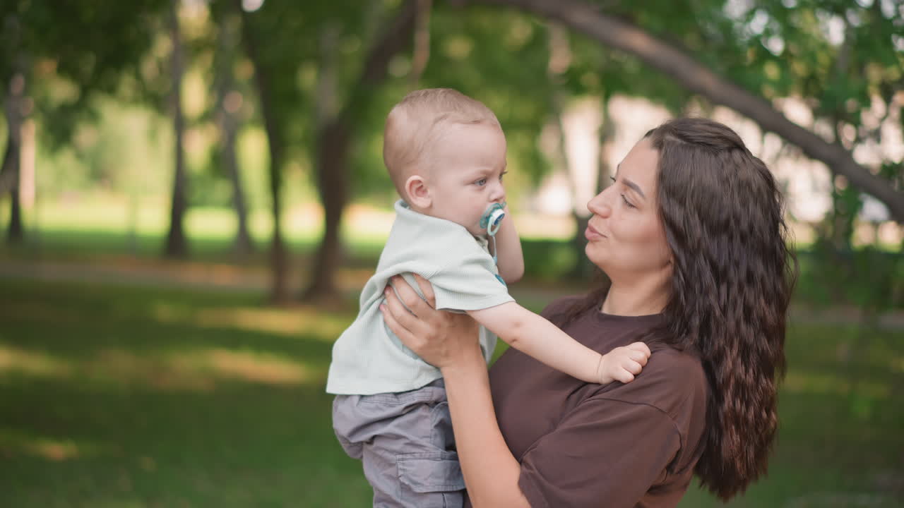 Abbraccio gioioso di una madre. Felice legame tra mamma e bambino. Madre premurosa supporta il figlio durante una giocosa visita al parco. Madre spensierata culla dolcemente il suo bambino felice in un lussureggiante parco verde