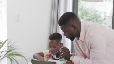 african american father helps son with homework at home using a tablet