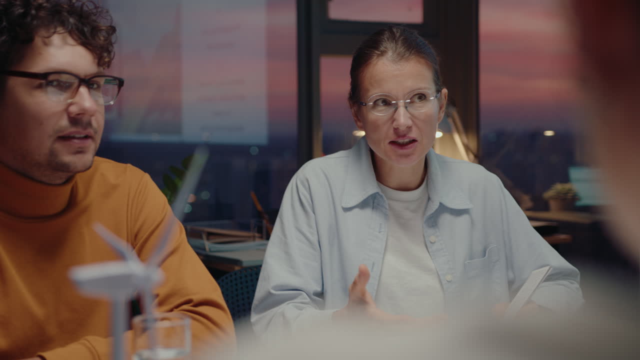 여성 엔지니어가 저녁에 사무실 회의에서 팀과 함께 재생 가능한 풍력 에너지 프로젝트를 논의합니다.