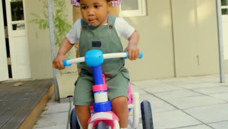 Front-view-of-cute-little-black-boy-riding-on-tricycle-in-back-yard-of-their-home-4k