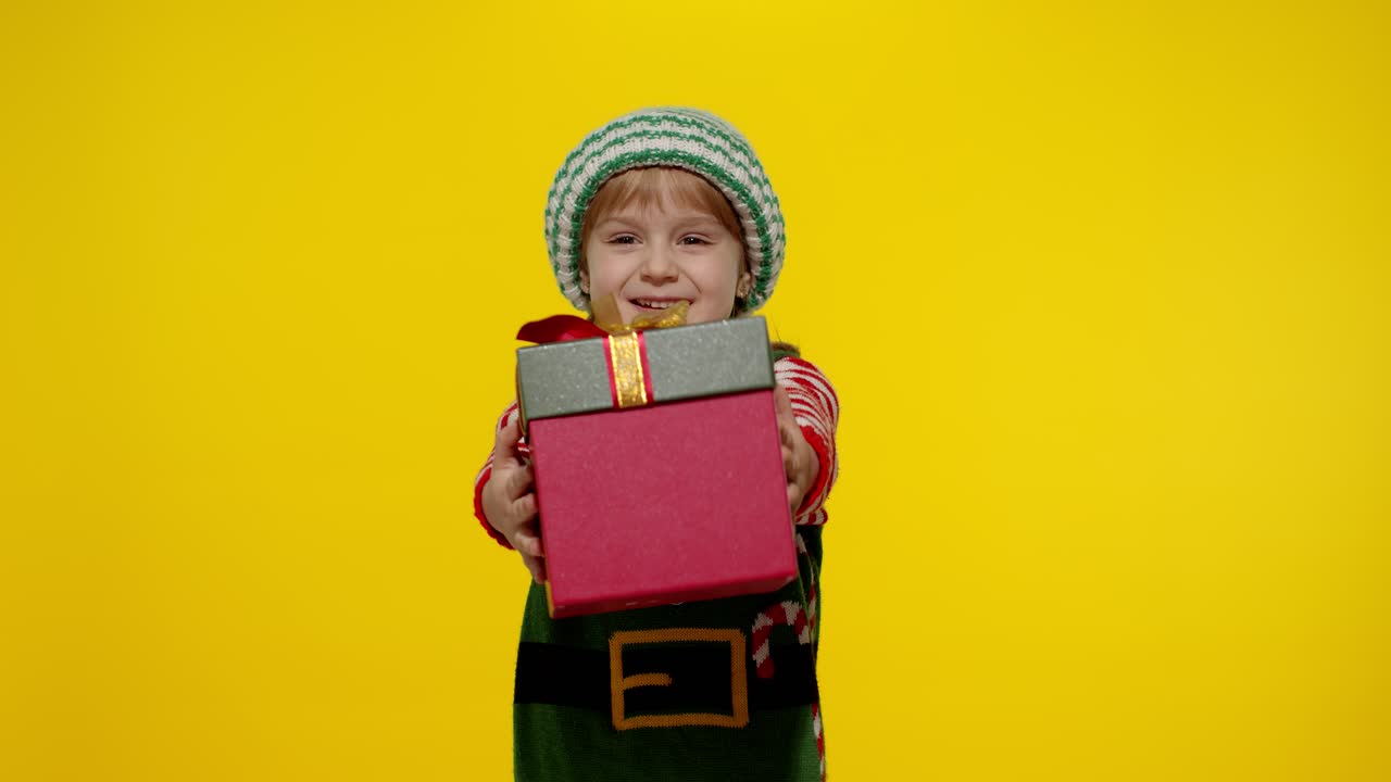 Dívka jako vánoční skřítek, pomocník Santa Clause, dává dárkovou krabici do kamery. Šťastné novoroční svátky.