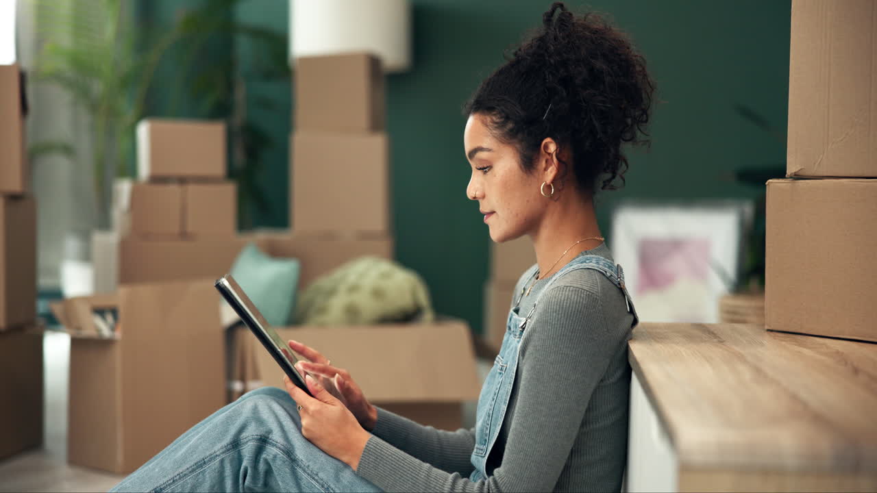 Young woman using tablet in new home with moving boxes
