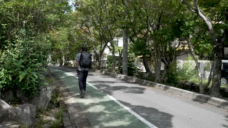 male solo traveller wearing backpack walking uphill along pedestrian path in mitaki, japan