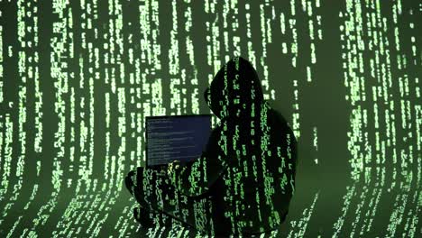 a hooded figure types on a laptop in a dark room filled with green digital rain. the silhouette blends into the matrix-like code, symbolizing stealth, intrusion, and cyber presence