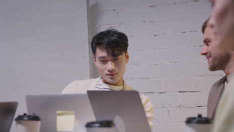 young man looking at laptop computer screen and talking with colleague during a team meeting