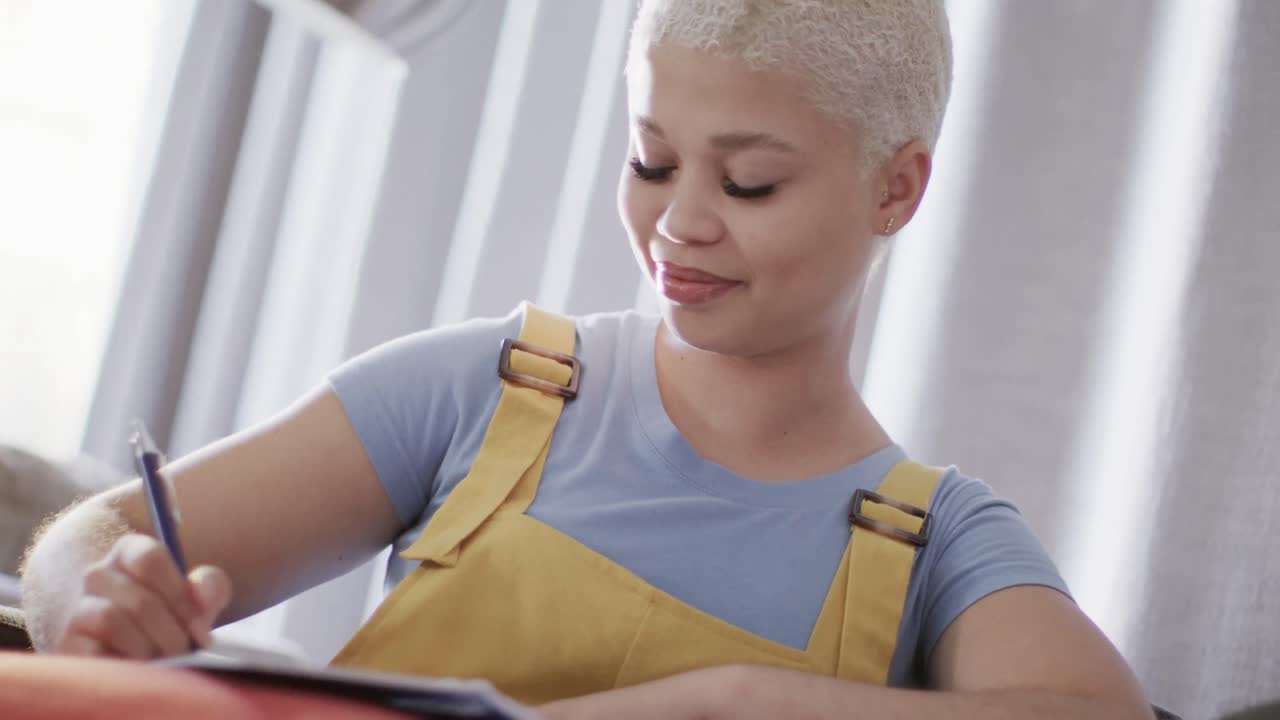 Happy biracial woman taking notes and sitting on couch in slow motion
