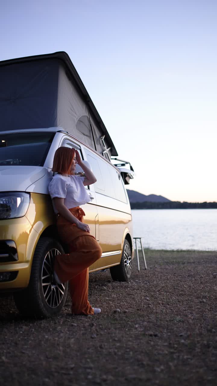 Giovane donna appoggiata a un camper vicino a un lago al tramonto
