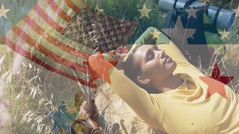 Animation-of-american-flag-over-biracial-woman-lying-in-mountains