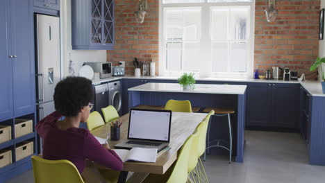 African-american-teenage-girl-at-kitchen-table-in-online-lesson-using-laptop-with-copy-space