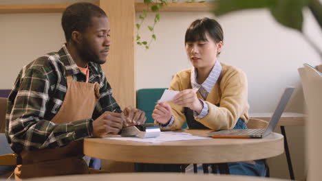 Two-Multiethnic-Coffee-Shop-Owners-Sitting-At-Table-And-Doing-Accounting-1