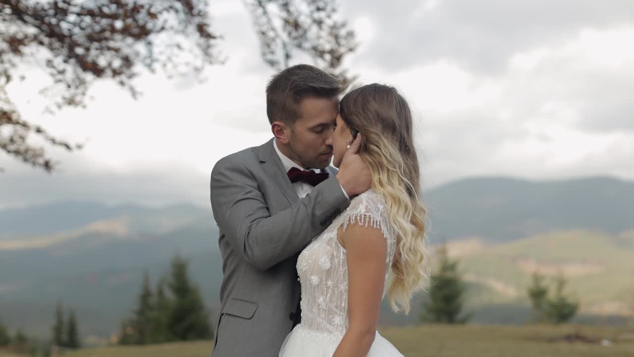 Lovely young newlyweds bride and groom embracing, making a kiss on mountain slope, wedding couple