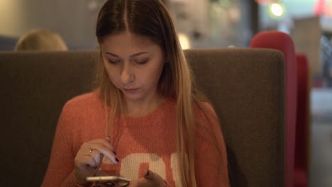 joven hermosa se sienta en un café trabaja en un teléfono inteligente 1