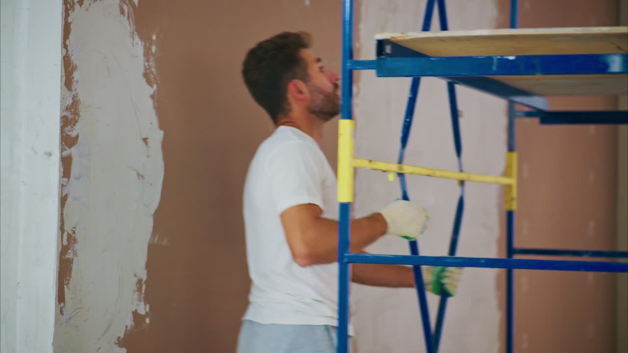 A Professional Worker on a Scaffold Prepares to Paint a Wall, Demonstrating Construction Techniques and Safety in a Renovation Project