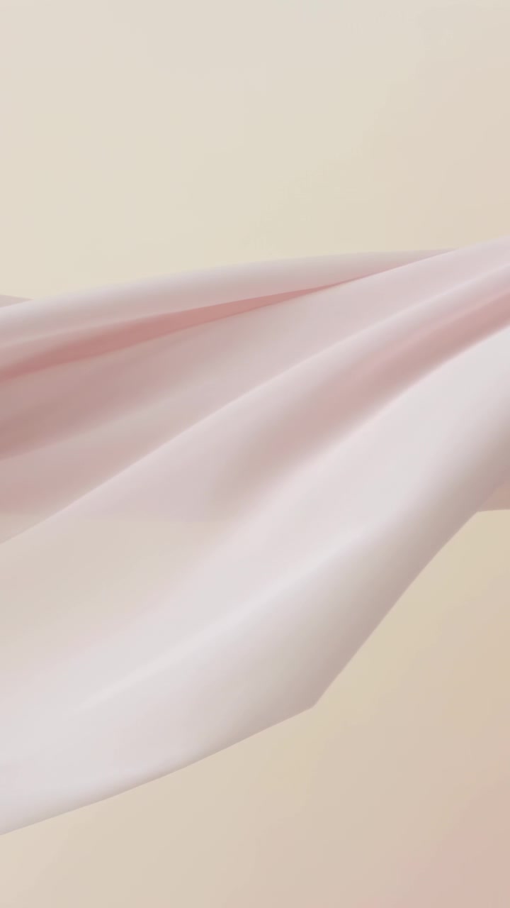 Vertical video: Floating pale pink satin fabric drifting across beige studio wall, moved by fan