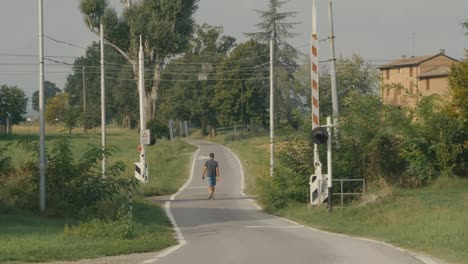 Ein-Mann-überquert-Zu-Fuß-Die-Gleise-Eines-Bahnübergangs-Auf-Einem-Feldweg-In-Der-Poebene,-Einer-Verträumten-Und-Friedlichen-Landschaft