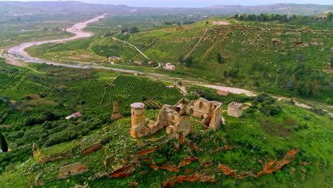 aerial forwarding shot of ruins of an old building over hilly terrain with a winding river flowing in the background in north of troina, sicily, italy at daytime