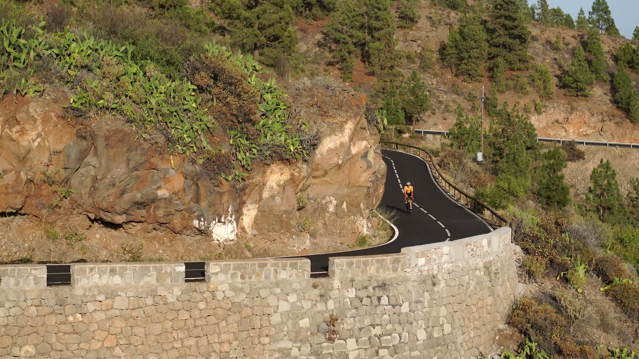 노란색 티셔츠를 입은 남성 자전거 타는 사람이 산의 높은 곳에 위치한 도로를 따라 성능 도로 자전거를 타고 있습니다.