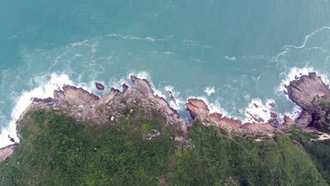 Aerial-view-of-a-jagged-rock-island,-surrounded-with-lush-green-nature-and-Hong-Kong-bay-water