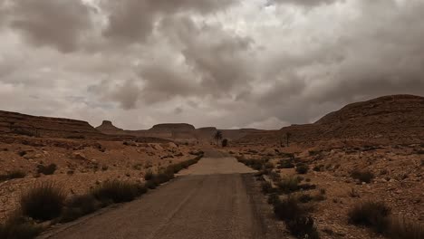 driving on desert road in tunisia with ksar guermessa troglodyte village in background cloudy day