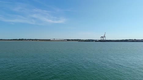 drone footage flying over harwich harbour with industrial cranes, shipping docks and coastal town buildings, clear blue sky, england