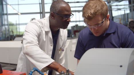 engineer teaching apprentice how to use machine in factory