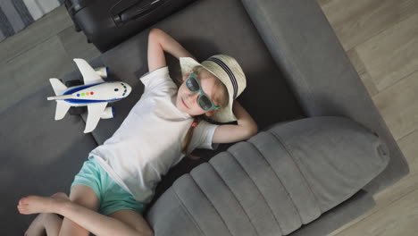 relaxed preschooler lies on sofa near airplane and suitcase