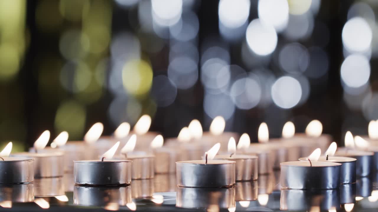 Video di una fila di lumini a candela con fiamme bianche e spazio per il testo con effetto bokeh su sfondo nero