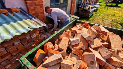 stacked used bricks with worker loading materials in sunny outdoor yard