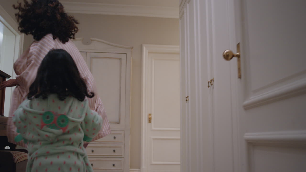 행복한 어린 소녀가 엄마와 딸을  ⁇ 고 놀고 집을 가로질러 달리고 엄마가 게임을 즐기고 아이와 함께 즐거운 주말 아침 4k 영상을 즐기고