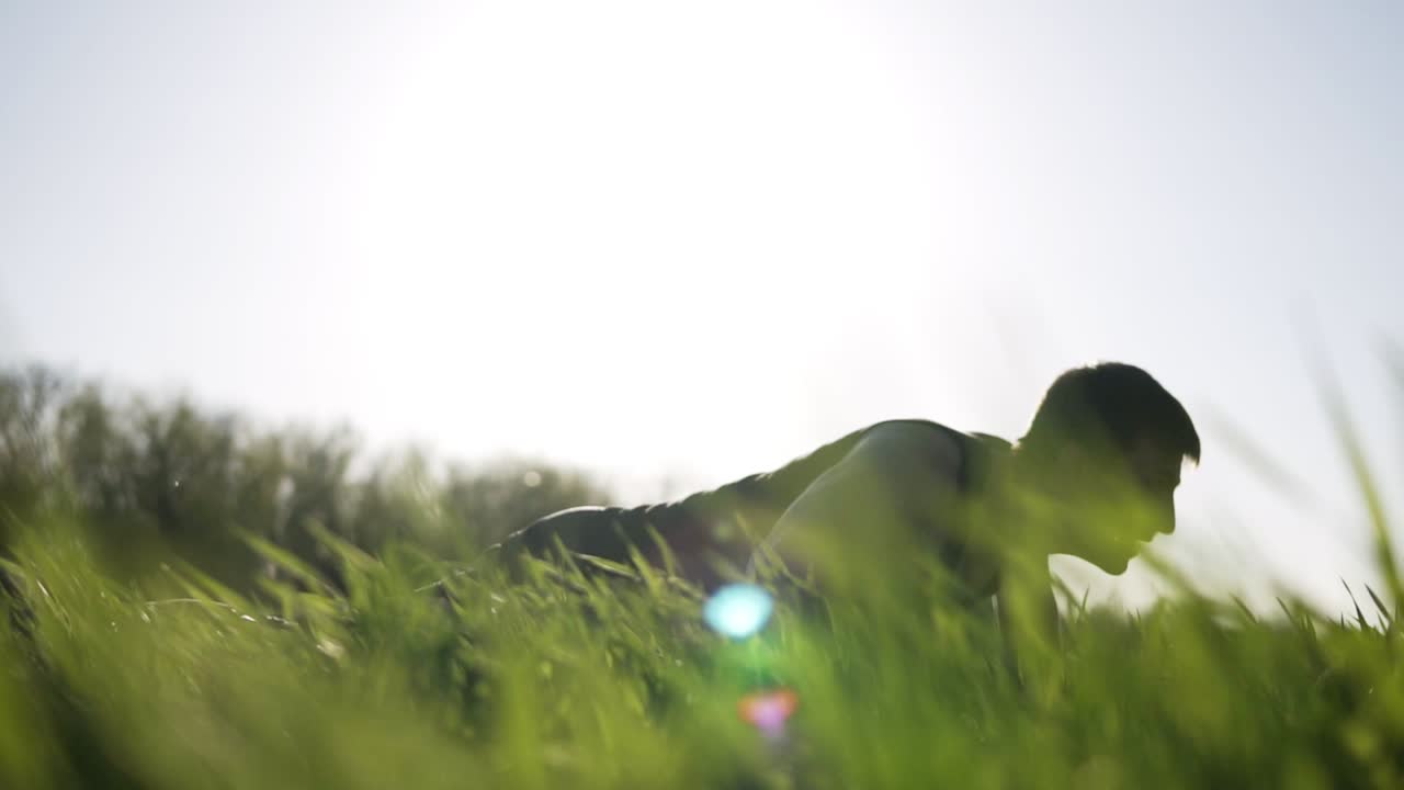 아래에서 찍은 영상. 한 남자가 푸시업을 연습하고 있습니다.  ⁇ 빛이 비추고 있습니다. 야외에서. 팔을 위로 펴고 푸시업을 하고 있습니다.