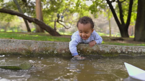 Boy-playing-with-water-in-fountain,-his-paper-ship-sailing-off