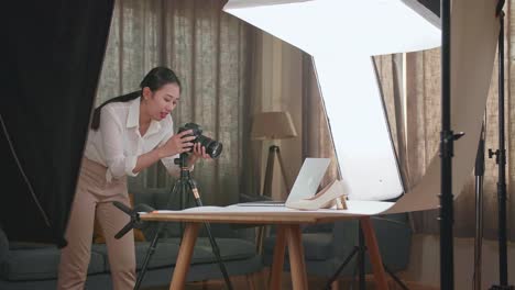 asian female photographer comparing photos on a laptop to camera while taking photos of women's shoes in home studio