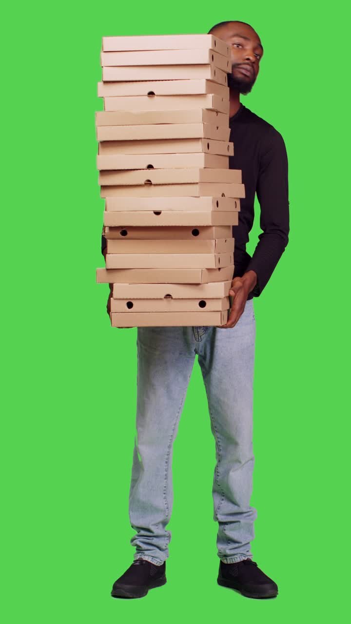 Vertical video: Front view of young person delivering big pile of pizza on camera