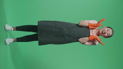 아시안 여성 집주인의 몸이 가득 차 있고, 앞옷을 입고, 몸짓을 보여주는 손, 손바닥, 와우라고 말하는, 그리고 녹색 스크린 스튜디오에서 미소 짓는