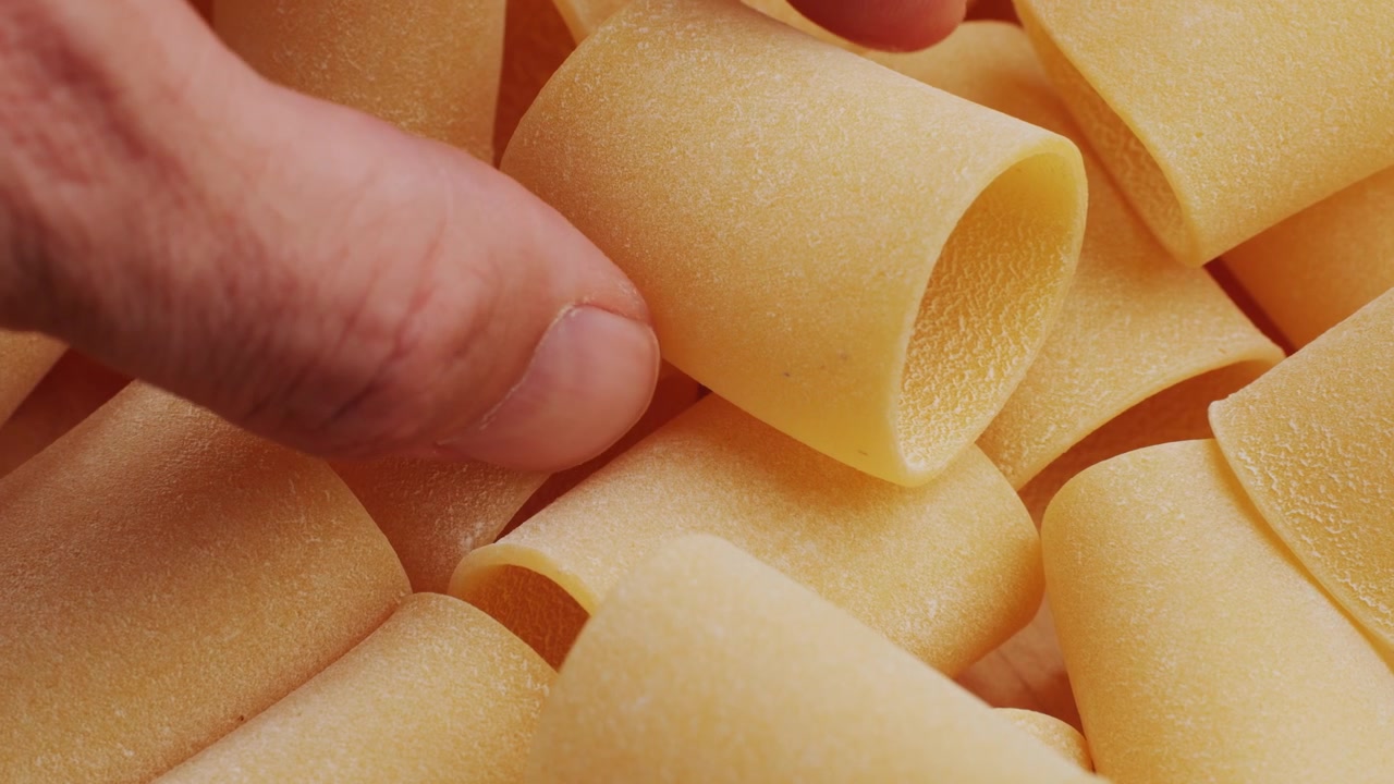 Primo piano di una mano che raccoglie paccheri secchi