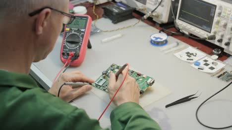 electronic equipment repair shop. the engineer technician solders the printed circuit board of an electronic device under a microscope.